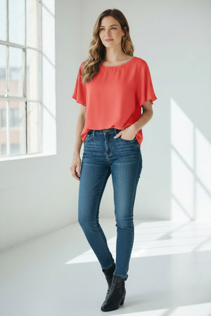 A woman with long, wavy blonde hair models the MEIMEIJ FLUTTER SLEEVE BLOUSE, paired with bold black floral print pants. The refined look is effortless and perfect for washable silk styles, set against a light textured background.