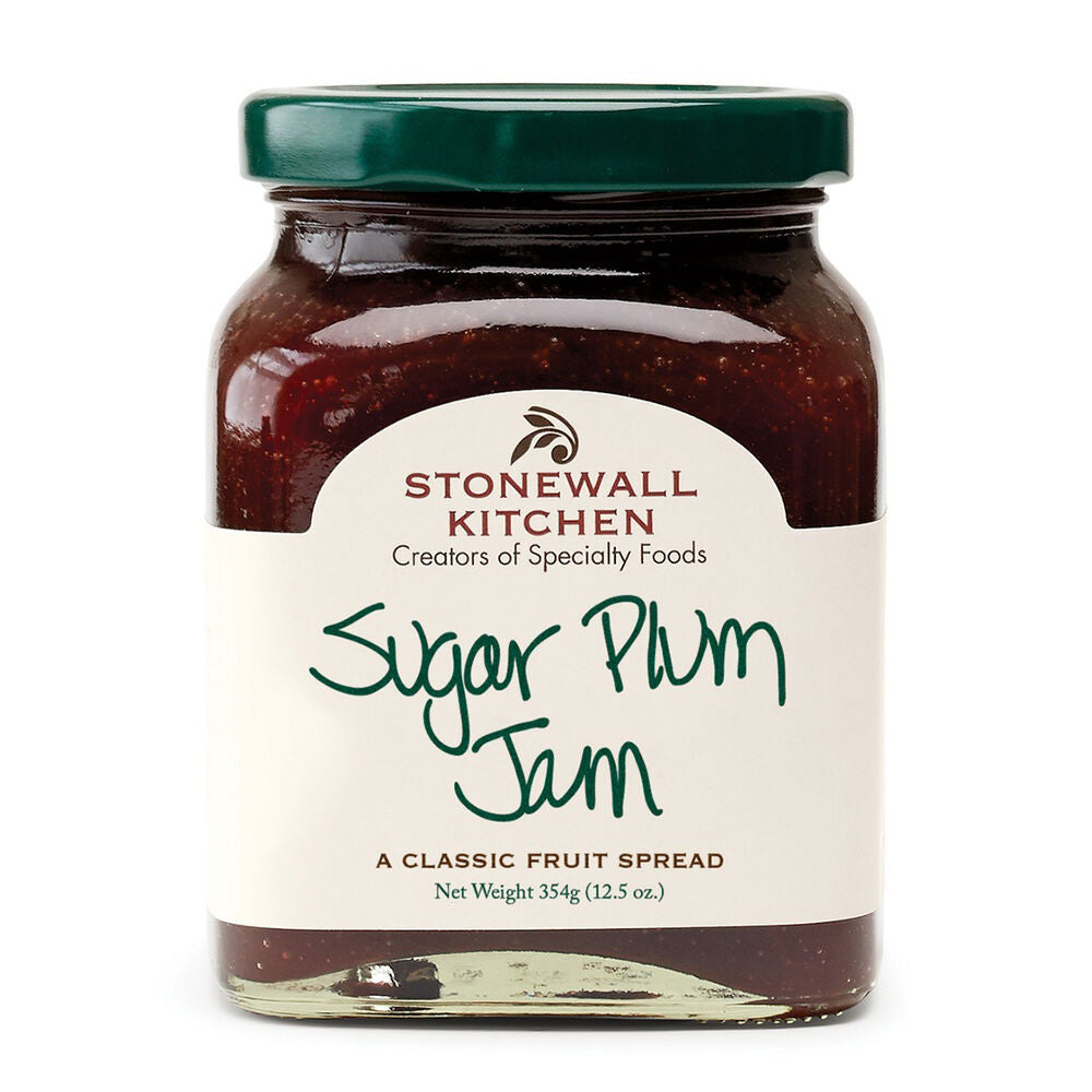 A jar of STONEWALL KITCHEN - SUGAR PLUM JAM is showcased, ideal for holiday treats. The label describes it as &quot;a classic fruit spread&quot; and has a net weight of 354g (12.5 oz). The jar comes with a green lid, and the jam inside is a deep red color.