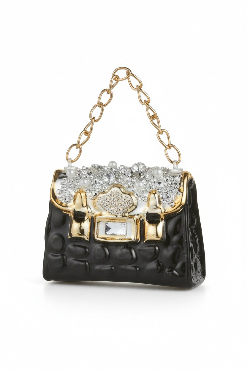 JEWELED PURSE ORNAMENT by RAZ IMPORTS, a miniature black glass handbag featuring gold trim, a metal chain handle, and rhinestone embellishments on the flap.