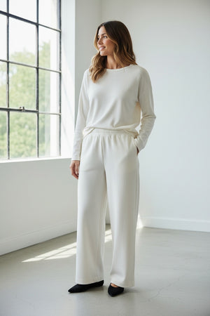 A person wears MEIMEIJ - PULL ON PANTS, featuring a wide-leg silhouette and elastic waistband, standing on a beige carpet in black shoes. These chic MEIMEIJ pants are made in Italy; the upper body is mostly out of frame.