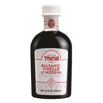 A small dark bottle of TOSCHI - BALSAMIC VINEGAR OF MODENA, produced in Italy by the ATALANTA CORPORATION. It features a white label with red text and decorative patterns, topped with a white cap. The label states &quot;Net 8.5 fl oz. (250 ml)&quot; at the bottom, indicating its aging process in oak barrels for a rich flavor.