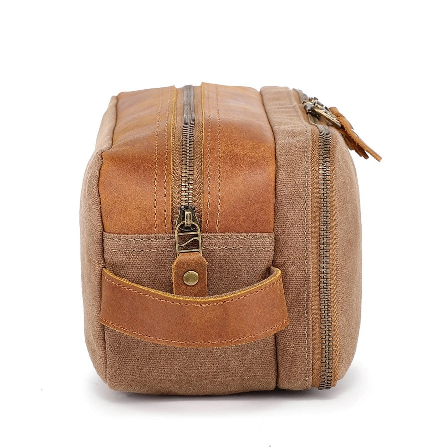 The TSD BRAND Turtle Ridge Toiletry Bag in khaki features leather accents, two zippered compartments, a side handle, and a small logo patch on the front pocket.