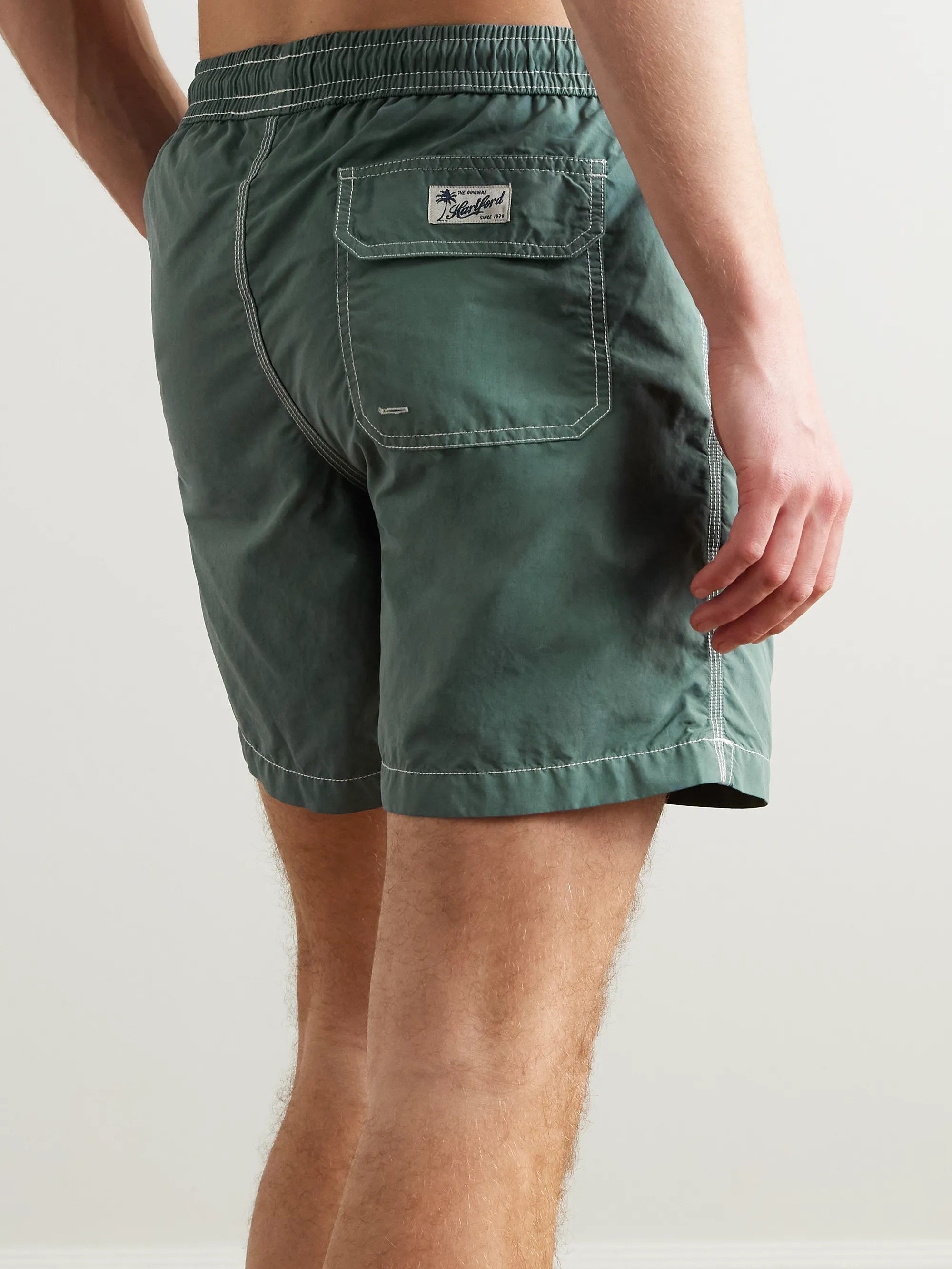 A pair of HARTFORD nylon swim trunks in Faded Kelly with white stitching and side pockets, shown flat on a light background. Includes travel pouch.