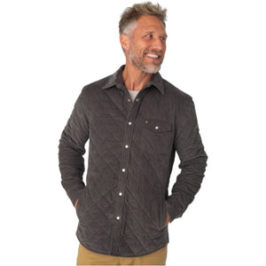 A smiling man with gray hair and a beard stands with his hands in his pockets against a plain white background, wearing tan pants and the CRIQUET Corduroy Quilted Shacket by CRIQUET.