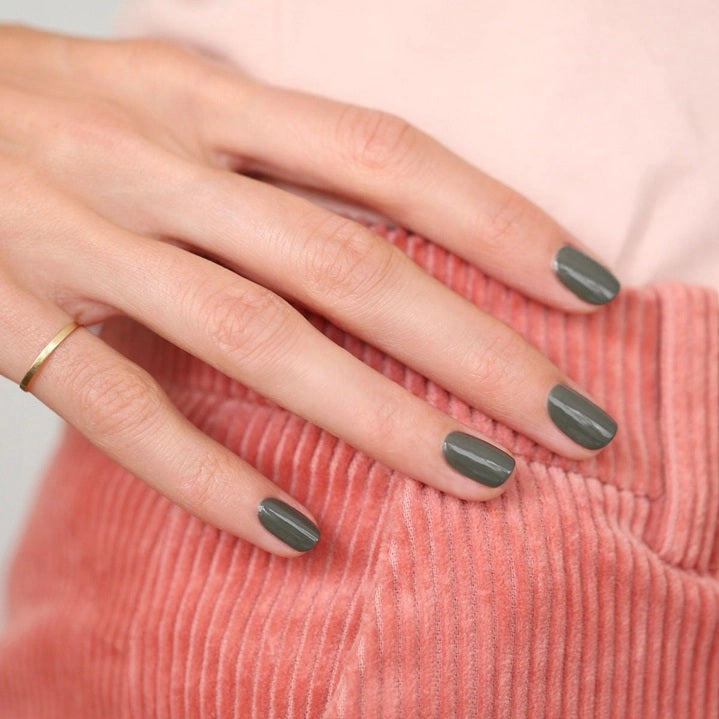A bottle of MANUCURIST INC GREEN™ Nail Polish in Khaki, featuring a black cap and a label that reads “NAIL POLISH KHAKI, green, QUICK DRY INTENSE COLOR.” This vegan nail polish delivers quick-drying, intense color for a modern look.
