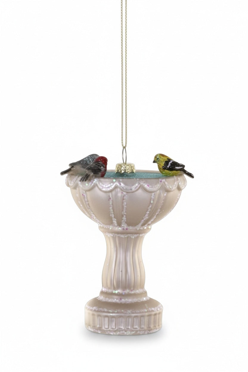 The CODY FOSTER BIRD BATH ORNAMENT features a white bath with two colorful birds perched on the edge, hanging by a gold string—a delightful holiday gift for collectors and design lovers.