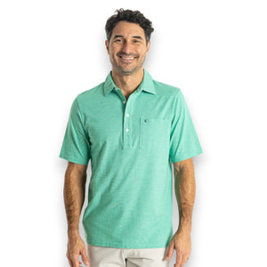 A person wears the CRIQUET Top-Shelf Players Shirt in Golf Green Microstripe with white buttons and a front pocket displaying a small embroidered logo; their face is partially out of frame.