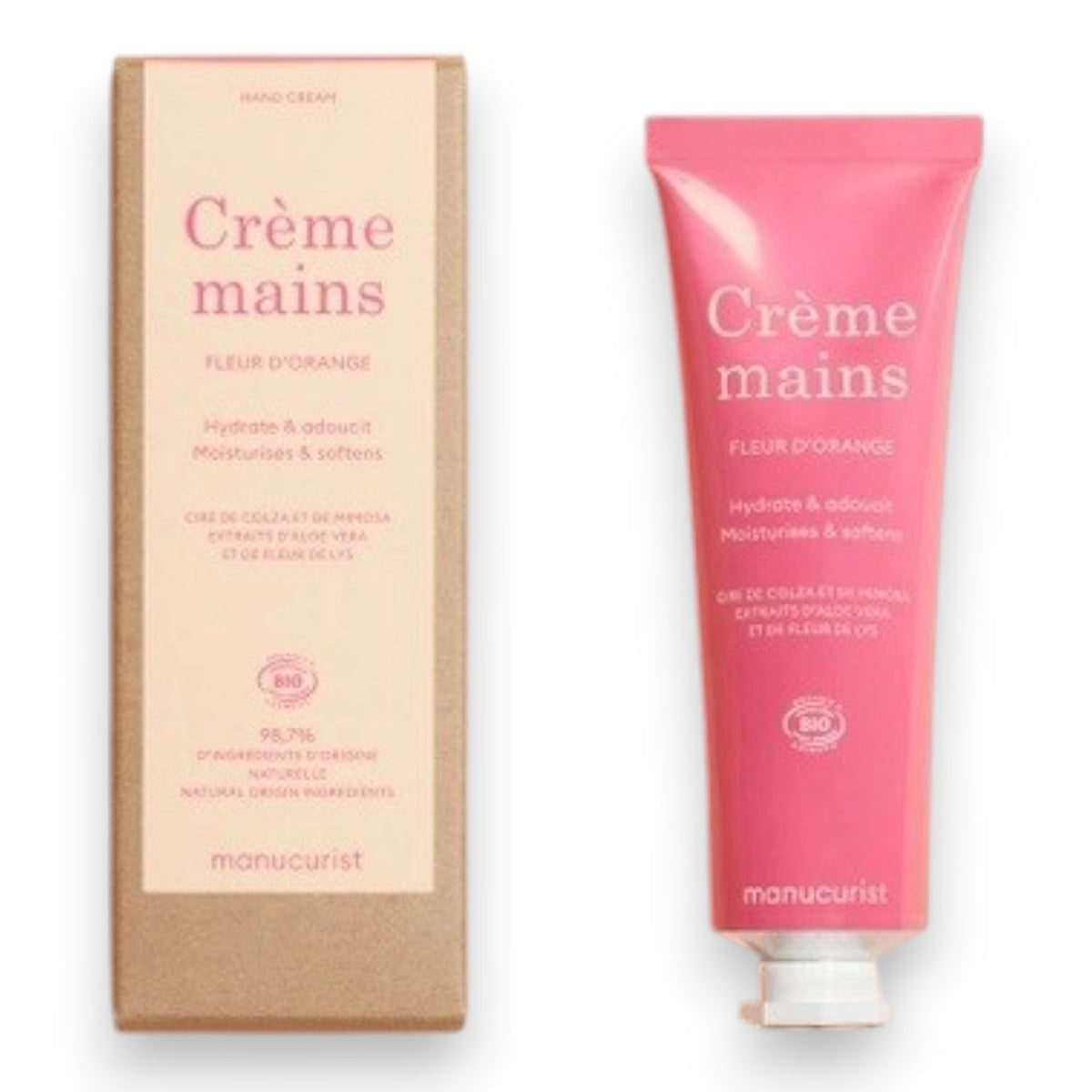Close-up of two hands with light skin; one is gently applying MANUCURIST - COSMOS ORGANIC HAND CREAM, ORANGE BLOSSOM by MANUCURIST INC to the back of the other against a neutral beige background. Ideal for hand and nail care, this organic moisturizer is formulated with natural ingredients to leave fingers nourished. The nails are perfectly groomed and finished with a subtle pale nude polish for an elegant touch.