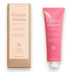 Close-up of two hands with light skin; one is gently applying MANUCURIST - COSMOS ORGANIC HAND CREAM, ORANGE BLOSSOM by MANUCURIST INC to the back of the other against a neutral beige background. Ideal for hand and nail care, this organic moisturizer is formulated with natural ingredients to leave fingers nourished. The nails are perfectly groomed and finished with a subtle pale nude polish for an elegant touch.