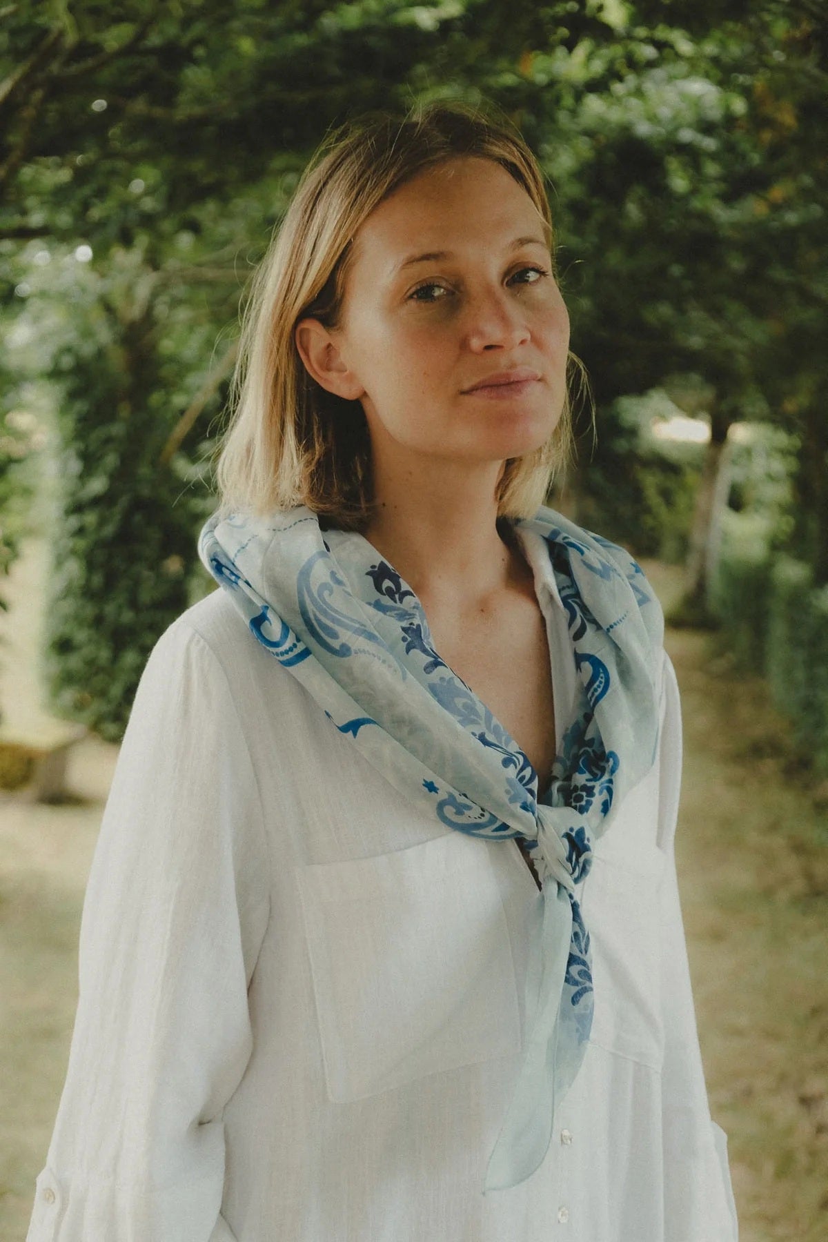 The MAISON LECOMTE - DINARD BANDANA SCARF IN COTTON VOILE by MAISON LECOMTE FLAMENT is a square, light blue cotton voile bandana adorned with an intricate paisley and floral pattern in shades of dark and light blue, elegantly displayed flat on a white background—an ideal accessory for any occasion.