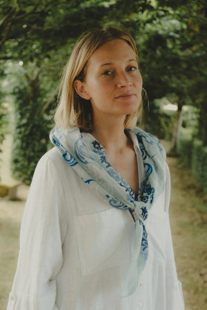 The MAISON LECOMTE - DINARD BANDANA SCARF IN COTTON VOILE by MAISON LECOMTE FLAMENT is a square, light blue cotton voile bandana adorned with an intricate paisley and floral pattern in shades of dark and light blue, elegantly displayed flat on a white background—an ideal accessory for any occasion.