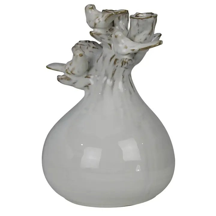 The HOMART CERAMIC VASE WITH BRANCH AND BIRD features white flowers and branches, set on a wooden surface with framed bird art and a woven basket against a light gray textured wall for a cozy touch.