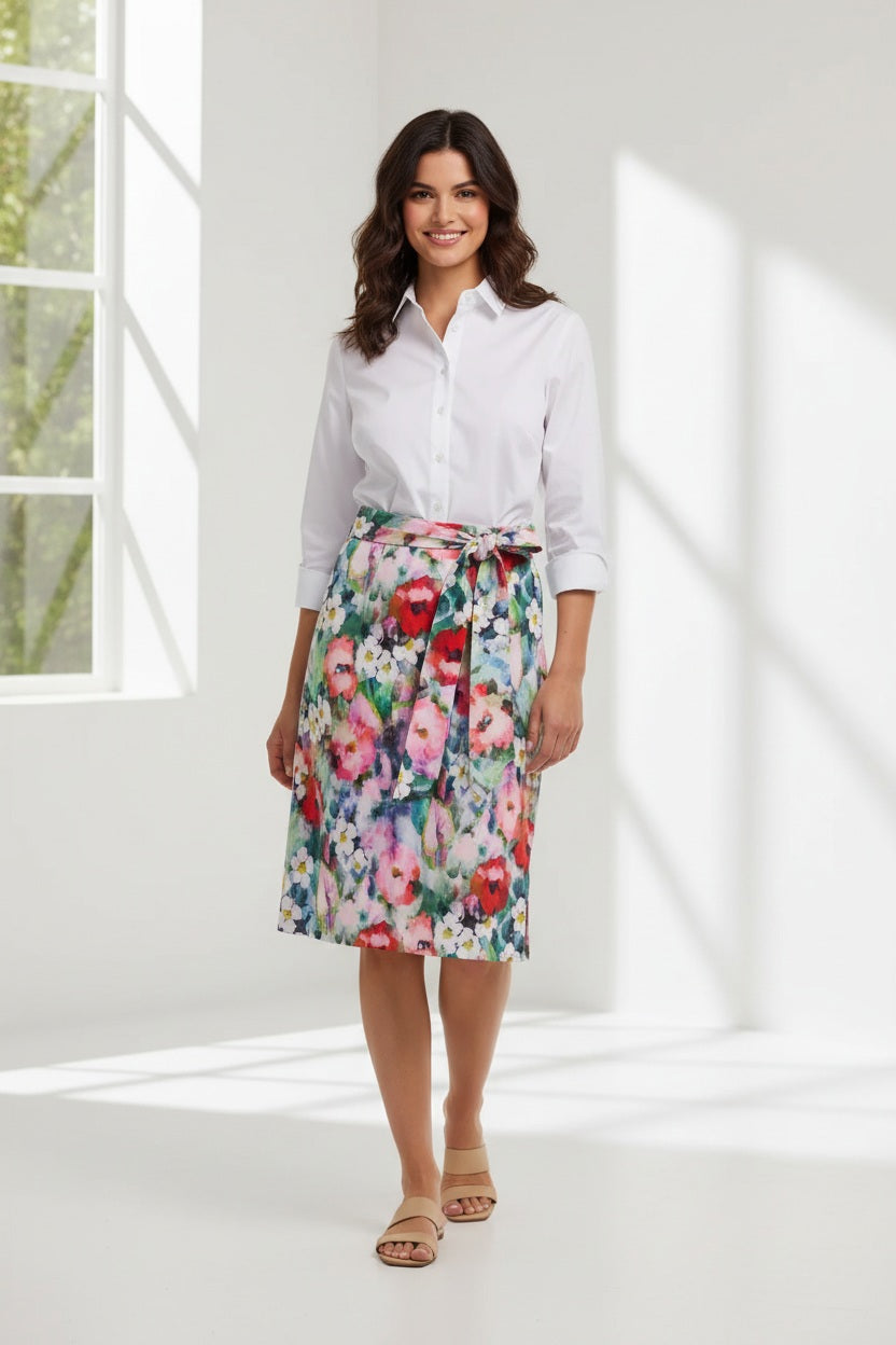 A woman faces forward in the HINSON WU CHARLOTTE 3/4 Sleeve Watercolor Garden Combo Dress, featuring a premium cotton-blend white button-up top and a colorful floral skirt with a matching tied belt. The background is plain and neutral.