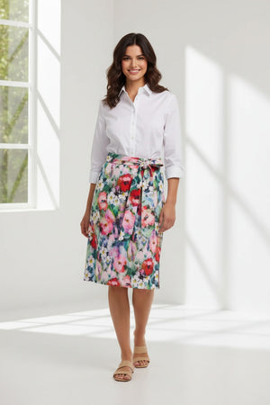 A woman faces forward in the HINSON WU CHARLOTTE 3/4 Sleeve Watercolor Garden Combo Dress, featuring a premium cotton-blend white button-up top and a colorful floral skirt with a matching tied belt. The background is plain and neutral.
