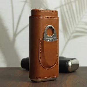 The AMERICAN LEATHER GOODS Leather Cigar Case with wood-lined humidor and cutter in brown sits on a wooden surface, while a black case rests behind. Leaf shadows appear on the wall in the background.