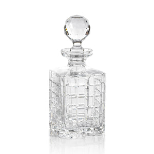 The BELMORE CRYSTAL GLASS WHISKEY & BRANDY DECANTER by ZODAX, featuring a faceted stopper and partially filled with whiskey, rests on a table beside matching barware—a glass and a pen.