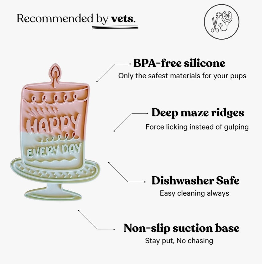 A pastel pink, cake-shaped HAPPY LICK MAT by BARKS & BROWNIES, crafted from food-grade silicone and featuring a candle on top with the words “HAPPY EVERY DAY,” displayed on a cake stand.