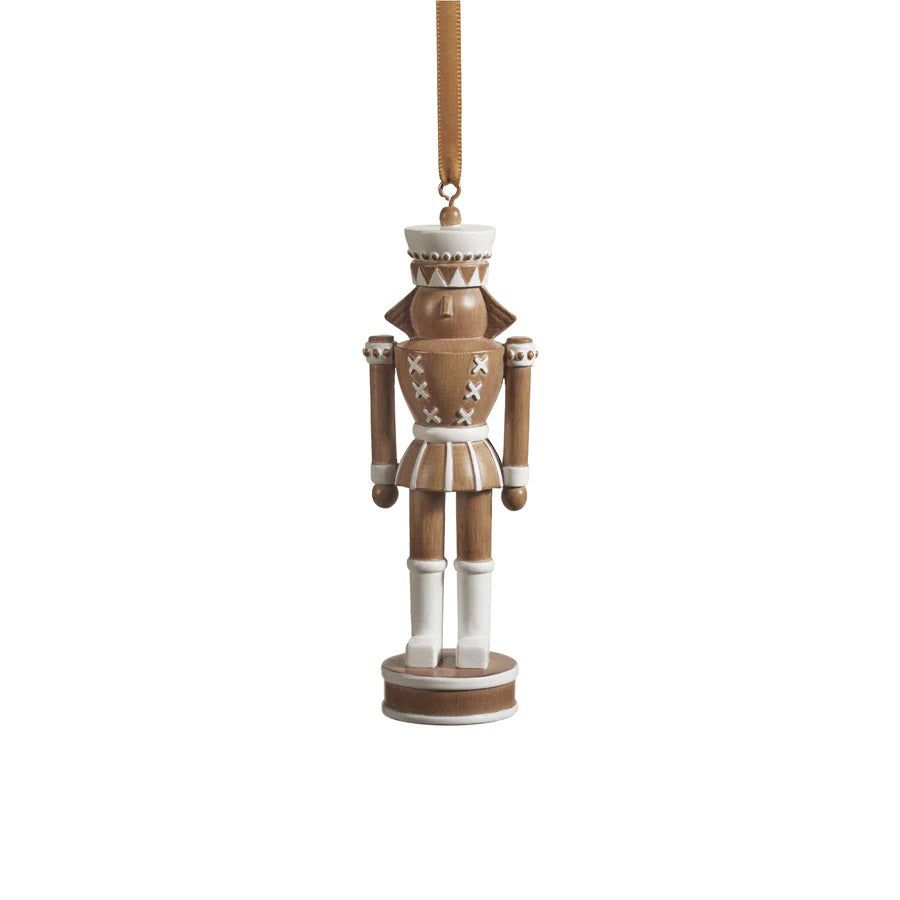 The ZODAX NUTCRACKER ORNAMENT is a beautifully crafted piece with a minimalist design, featuring an elegant brown and white color scheme. It stands upright at an optimal size, showcasing a flat hat, detailed uniform, and is elegantly suspended by a gold ribbon, making it ideal for any display.