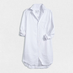 The FRANK AND EILEEN - MARY SHIRTDRESS IN TATTERED DENIM from FRANK & EILEEN is showcased against a textured, off-white background. This long-sleeved dress boasts a collared neckline, a single chest pocket, and a slightly curved hemline. The sleeves are rolled up neatly, making it an ideal favorite for all four seasons.