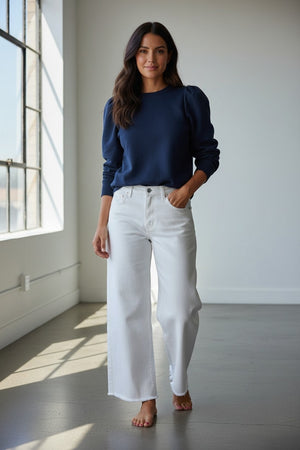 A person with long hair embraces comfort and individuality, wearing a KMJ SHIRTS Cooper Sweatshirt in gray with a white bow. Metallic sequin pants and silver shoes complete the look as they stand among disco balls on the floor against a plain background.