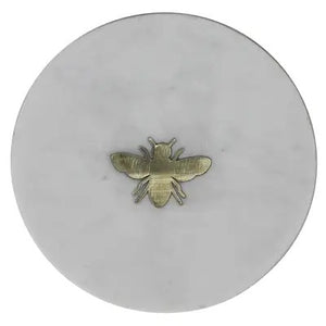 The HOMART MARBLE TRAY INLAID WITH BRASS BEE is a round, white marble tray featuring a small brass bee at the center and measures 6 inches in diameter.