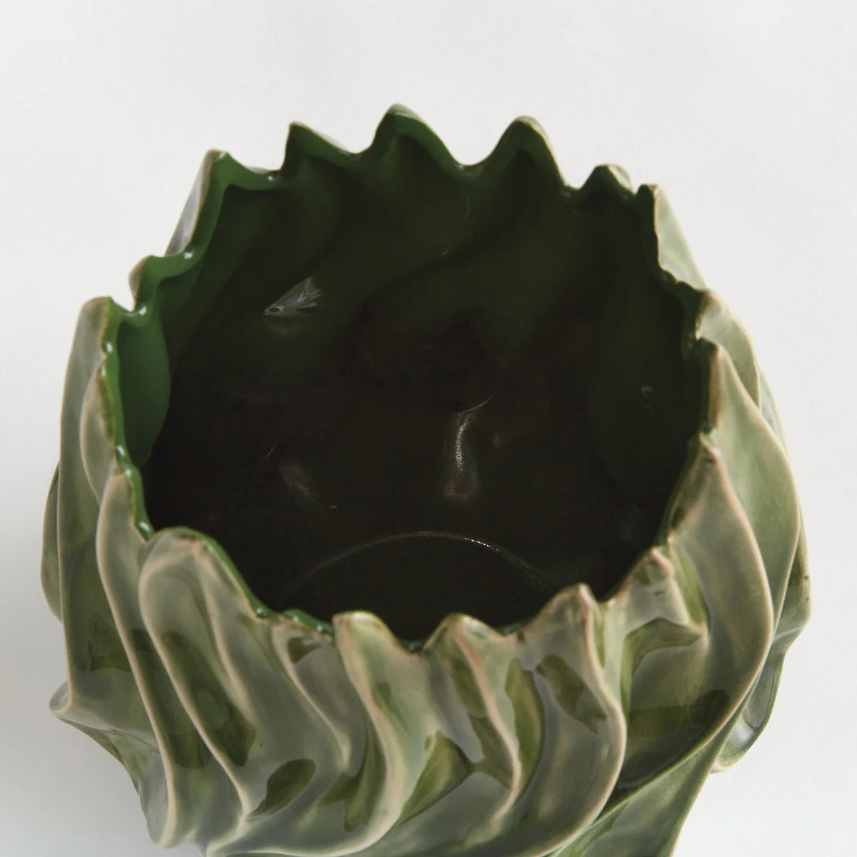 The NAPA HOME AND GARDEN - GREEN CALLISTA VASE, MEDIUM features a sculptural design with glossy green handcrafted ceramic, showcasing wavy, flame-like edges and ridges that evoke the look of abstract leaves or flames. A high-gloss reactive glaze accentuates its flowing, organic exterior shapes, while the interior is finished in a rich dark green.