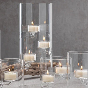 Five ZODAX SUSPENDED GLASS TEALIGHT HOLDER - EXTRA LARGE candle holders with floating tealights are arranged on a gray surface, with driftwood in the background. The windproof holders vary in height for an elegant display.