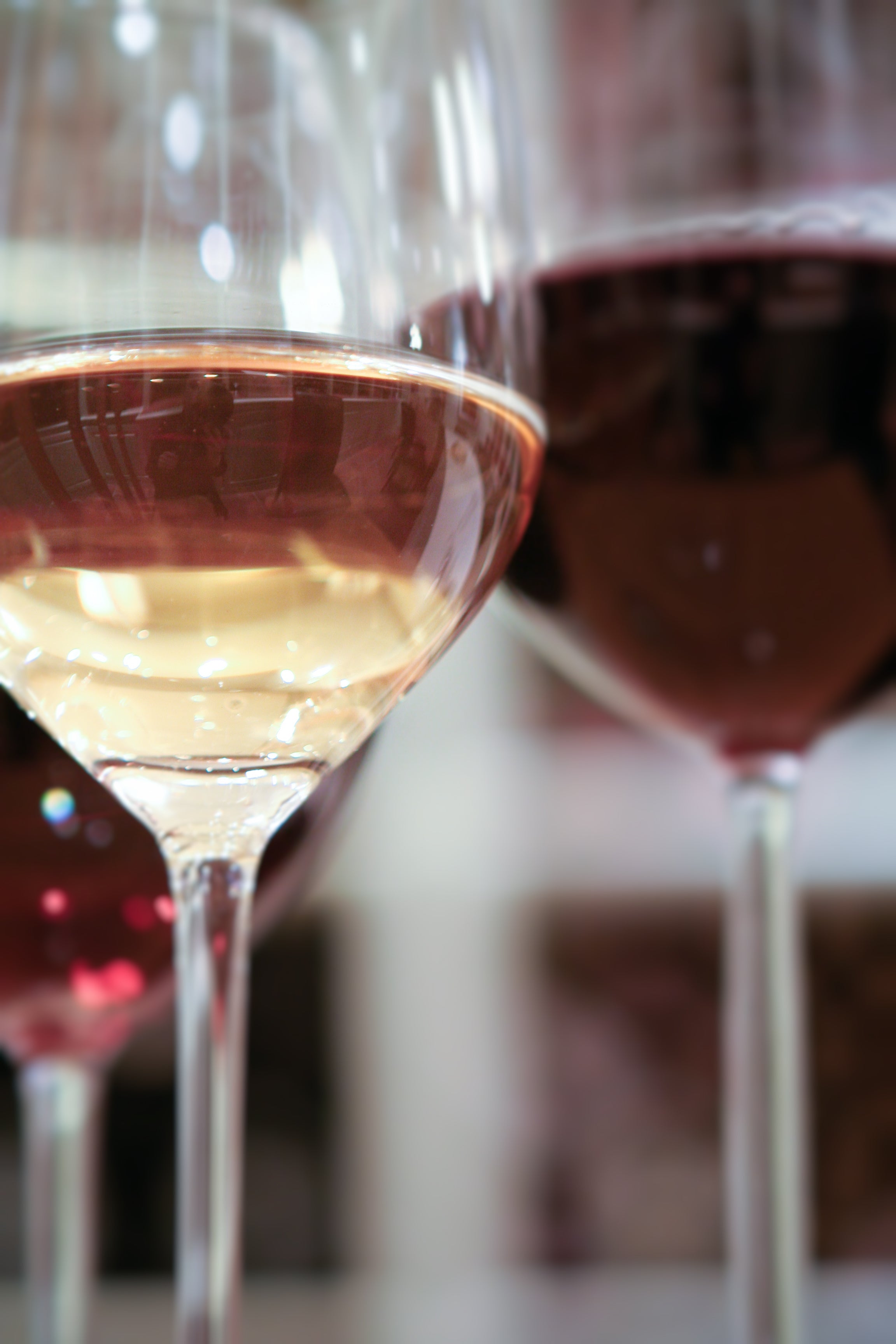 Close-up of three wine glasses, each filled with different types of wine—one with white wine, one with rosé, and one with red wine. The background is softly blurred.