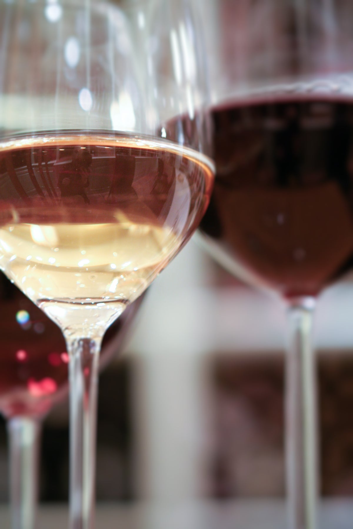Close-up of three wine glasses, each filled with different types of wine—one with white wine, one with rosé, and one with red wine. The background is softly blurred.
