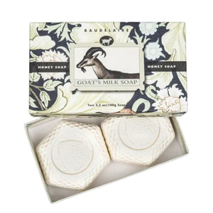 An open BAUDELAIRE - GOATS MILK HONEY SOAP 3.5oz 2 Bar Gift Box displays two hexagonal white soaps, ideal for sensitive skin. The cream and black box features a decorative floral print and an illustration of a goat.