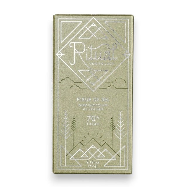 A green RITUAL CHOCOLATE - FLEUR DE SEL CHOCOLATE BAR 70% CACAO with silver geometric designs and text on the wrapper, shown on a white marble background.