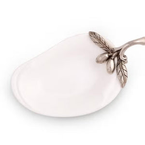 The VAGABOND HOUSE - OLIVE OIL SERVER/SPOON REST is a white, pear-shaped ceramic platter featuring a twig-like ornate metal handle adorned with pewter olives and small fruits. The handle is attached to the narrow end for an elegant touch to this minimalist design.