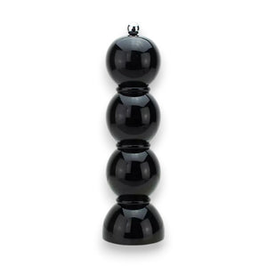 A vibrant display of ADDISON ROSS LONDON - BOBBIN SALT OR PEPPER MILL 24CM grinders in various shades such as pink, red, blue, orange, yellow, green, white, and a striking black lacquered finish. They are arranged on two shelves against a muted green background alongside various serving bowls.