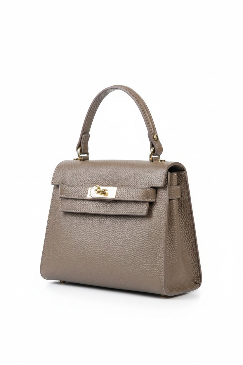 The LE BORSETTE LEATHER SATCHEL BAG is a small, structured satchel-shaped handbag in light pink, featuring a gold clasp at the front. It boasts a single top handle, an adjustable shoulder strap, and two gold-tone hardware pieces on either side of the handle. The textured leather adds to its luxurious and elegant appearance against the plain white background.