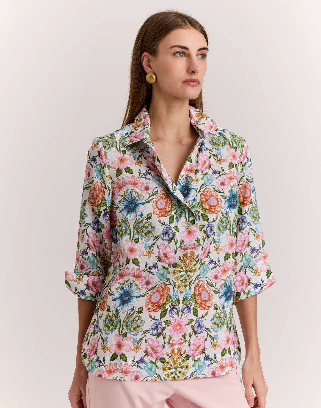 A woman with straight brown hair wears the HINSON WU - CHARLOTTE 3/4 SLEEVE LINEN SHIRT IN BOTANIQUE PRINT, paired with light pink pants, standing against a plain light background.