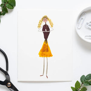 The PETAL PEOPLE PRESS - GRATITUDE CARD features a creative drawing of a girl made from dried leaves and petals on white paper, styled as botanical art, and shown on a white table with paper clips, a black tool, and green leaves.