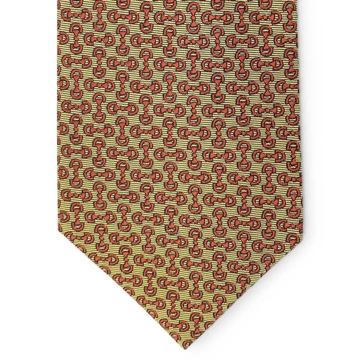 A close-up of the BIRD DOG BAY PETER-BLAIR - HORSEBIT SILK TIE IN YELLOW, featuring a handmade New York woven silk construction with a repeating pattern of small red horseshoes and horse heads on a yellow background. The tie has a pointed tip at the bottom.