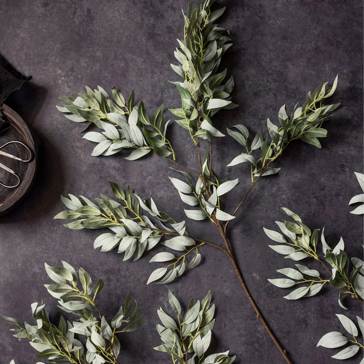 The ABIGAIL AHERN - WILLOW EMERALD features a single stem of artificial willow foliage with multiple branches and elongated green leaves, presented against a white background.