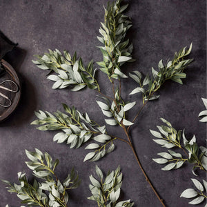 The ABIGAIL AHERN - WILLOW EMERALD features a single stem of artificial willow foliage with multiple branches and elongated green leaves, presented against a white background.