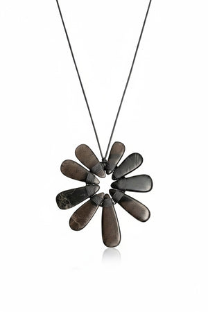 A mannequin wears a shaggy beige jacket paired with the ANN LIGHTFOOT Nine Petal Smokey Quartz Flower Necklace, which features a modern black cord and a bold, dark metallic floral pendant.