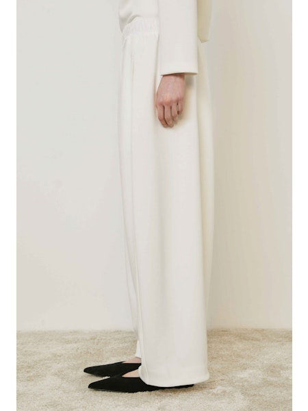 A person wears MEIMEIJ - PULL ON PANTS, featuring a wide-leg silhouette and elastic waistband, standing on a beige carpet in black shoes. These chic MEIMEIJ pants are made in Italy; the upper body is mostly out of frame.