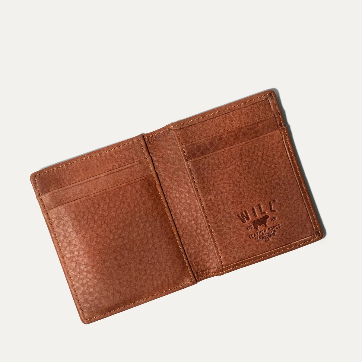 The WILL LEATHER GOODS Classic Money Clip sits atop an open full-grain leather wallet, both in brown, showcasing card slots against a plain light background.
