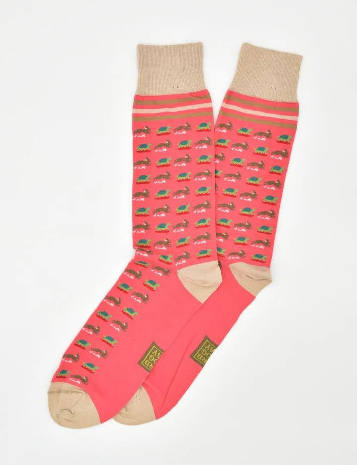 BIRD DOG BAY - TORTOISE &amp; HARE SOCKS IN CORAL by BIRD DOG BAY: Mid-calf socks in coral with beige toes, heels, and cuffs, featuring a whimsical repeating tortoise and hare pattern. Socks are laid flat on a white background.