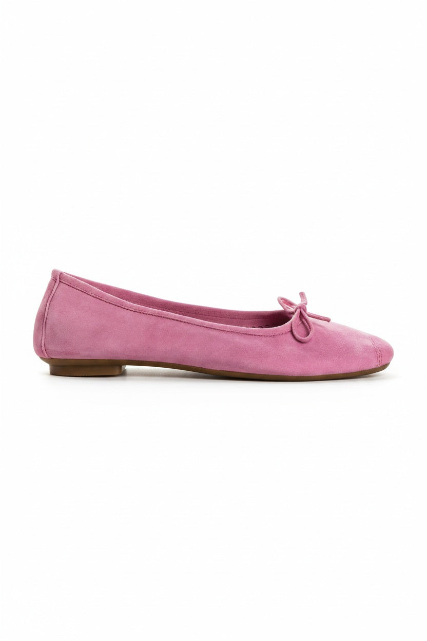 A close-up of the REQINS - HARMONY SUEDE BALLERINA FLATS IN PINK, featuring a bow detail on the front, photographed on a light surface—an elegant update to this classic women’s shoe by REQINS.