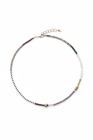 The ALICE RISE - PEARL MIXED MEDIA NECKLACE by ALICE RISE features small, multicolored vintage glass beads arranged in sections and finished with a 14k gold-filled clasp, displayed in a circle on a textured light blue surface.