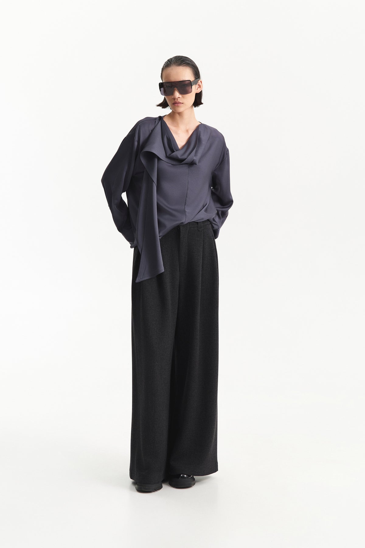 A person is shown from the shoulders down against a plain white background, wearing ELEH - BLACK PALAZZO TROUSERS by ELEH styled with black shoes and a loose-fitting, long-sleeve top.