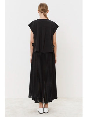 Against a plain white backdrop, a person models the MEIMEIJ Navy Plisse Dress. Paired with white pointed shoes, this minimalistic ensemble epitomizes versatile style. Their expression is neutral, enhancing the understated elegance of the look.