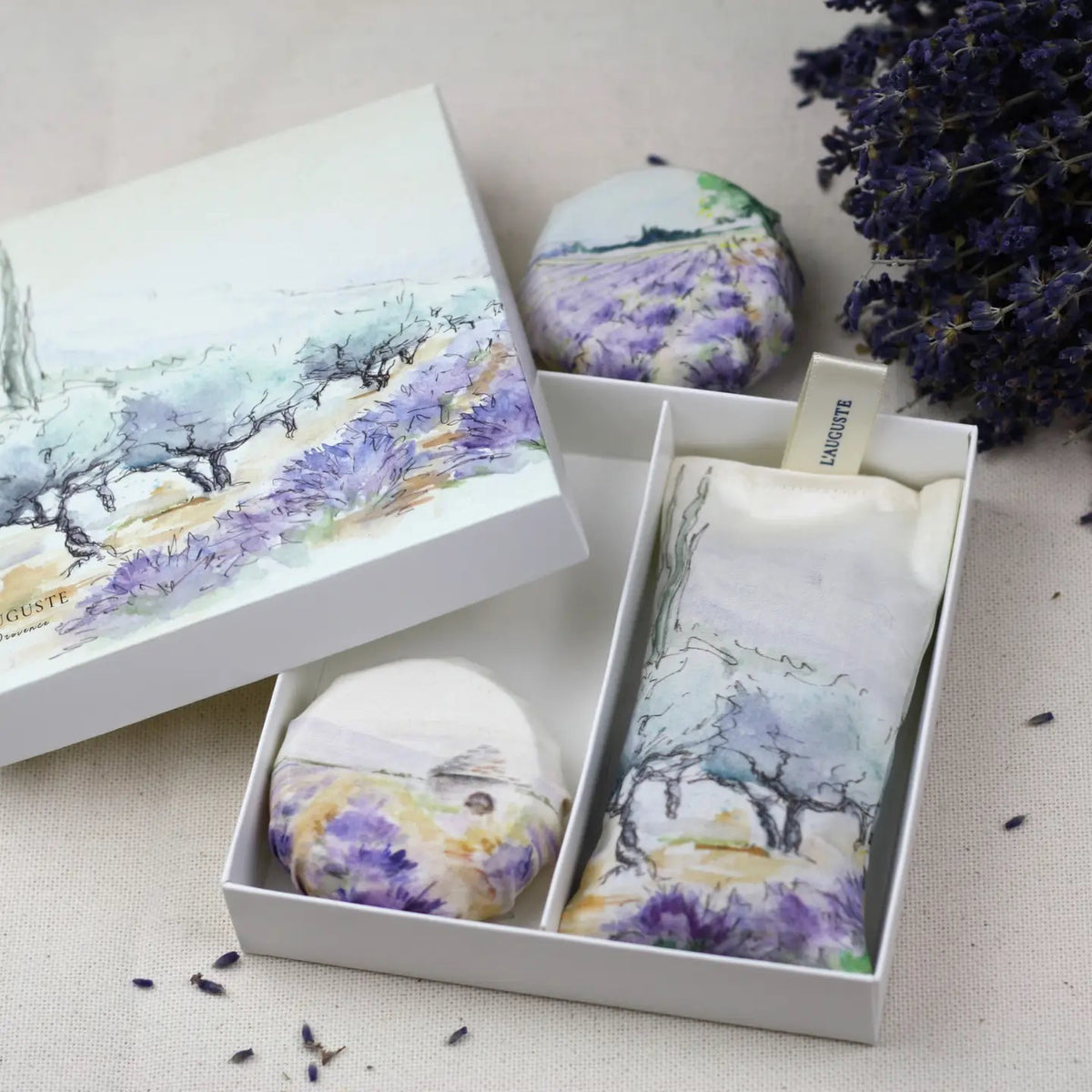 The L&#39;AUGUSTE PROVENCE - SUMMER IN PROVENCE gift box includes a lavender sachet, two round pouches, and dried Provence lavender, each featuring artwork inspired by scenic lavender fields.