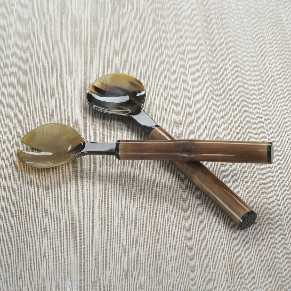 The ZODAX BAMBOO AND HORN SERVING SET features a spoon and slotted spoon with polished, horn-comb style handles in brown and black, elegantly crossed on a light textured surface.