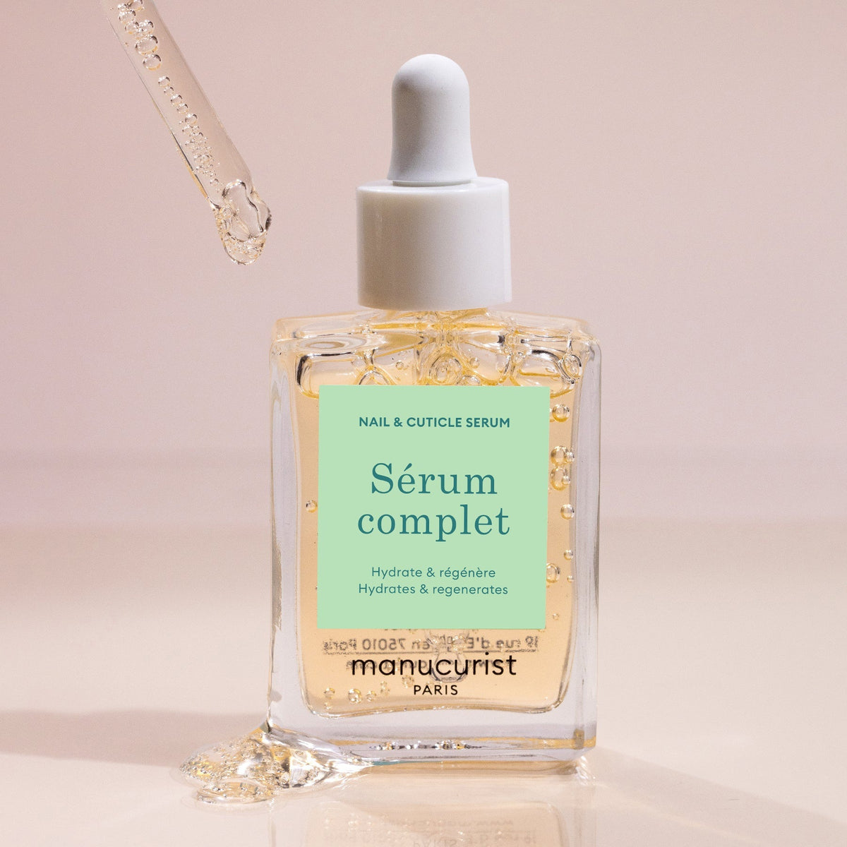 A clear glass dropper bottle labeled “SERUM COMPLET” with light blue and beige accents contains MANICURIST INC’s SERUM COMPLET NAIL HYDRATING SERUM, a transparent formula designed to hydrate and strengthen nails and cuticles.